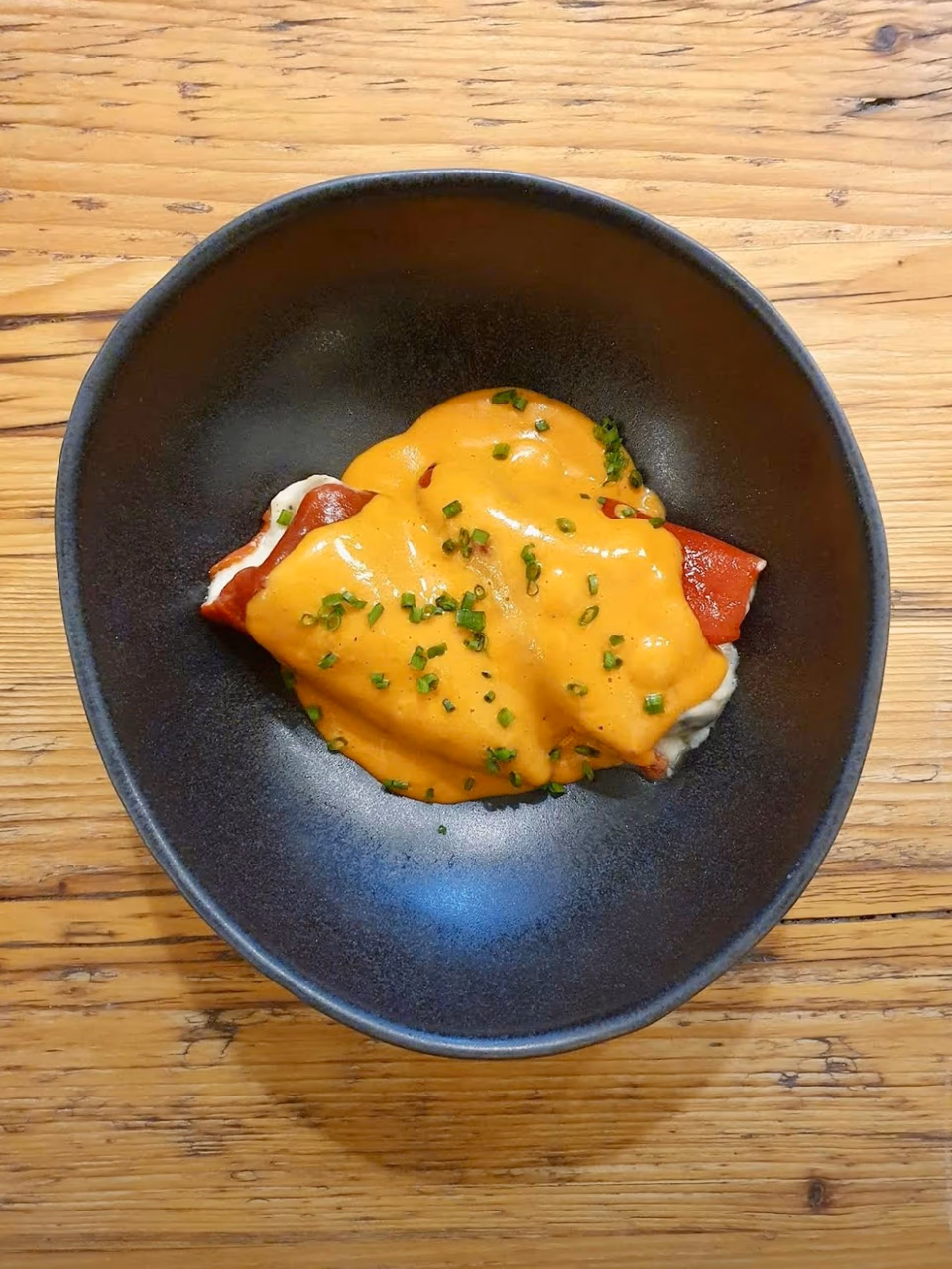 Gefüllter Pimiento mit cremiger Sauce auf dunklem Teller