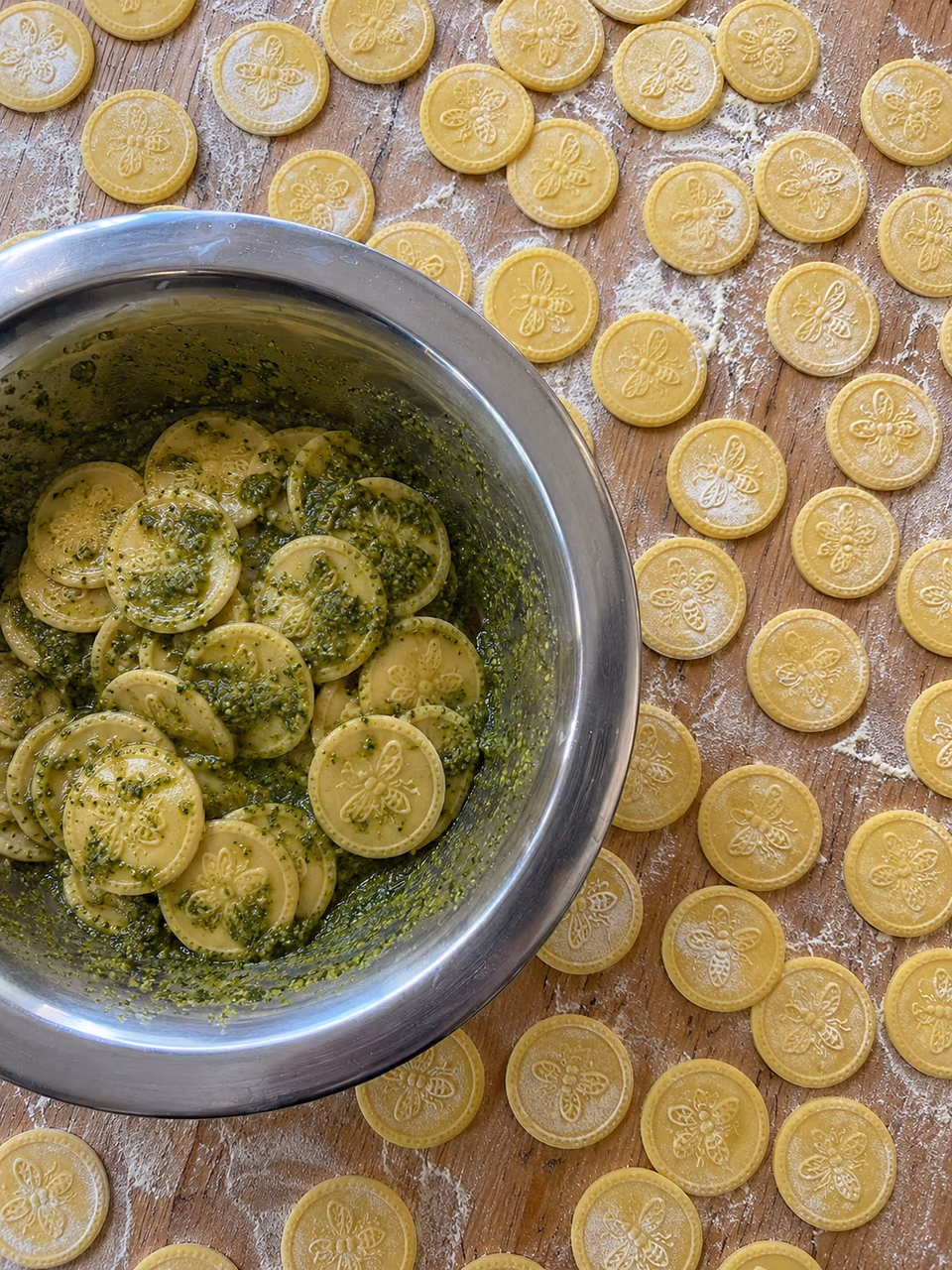 Geprägte Corzetti auf einem Holzbrett, daneben eine Schüssel mit Pesto Genovese
