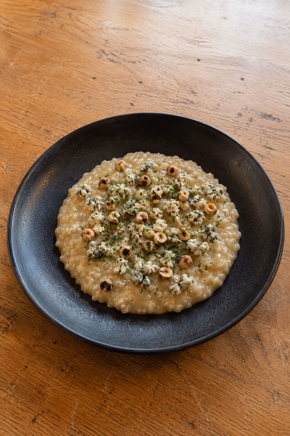 Risotto al Gorgonzola mit piemontesischen Haselnüssen auf einem dunklen Teller